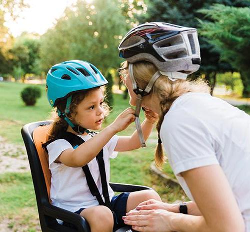 一名儿童坐在自行车后座上帮助母亲系好头盔